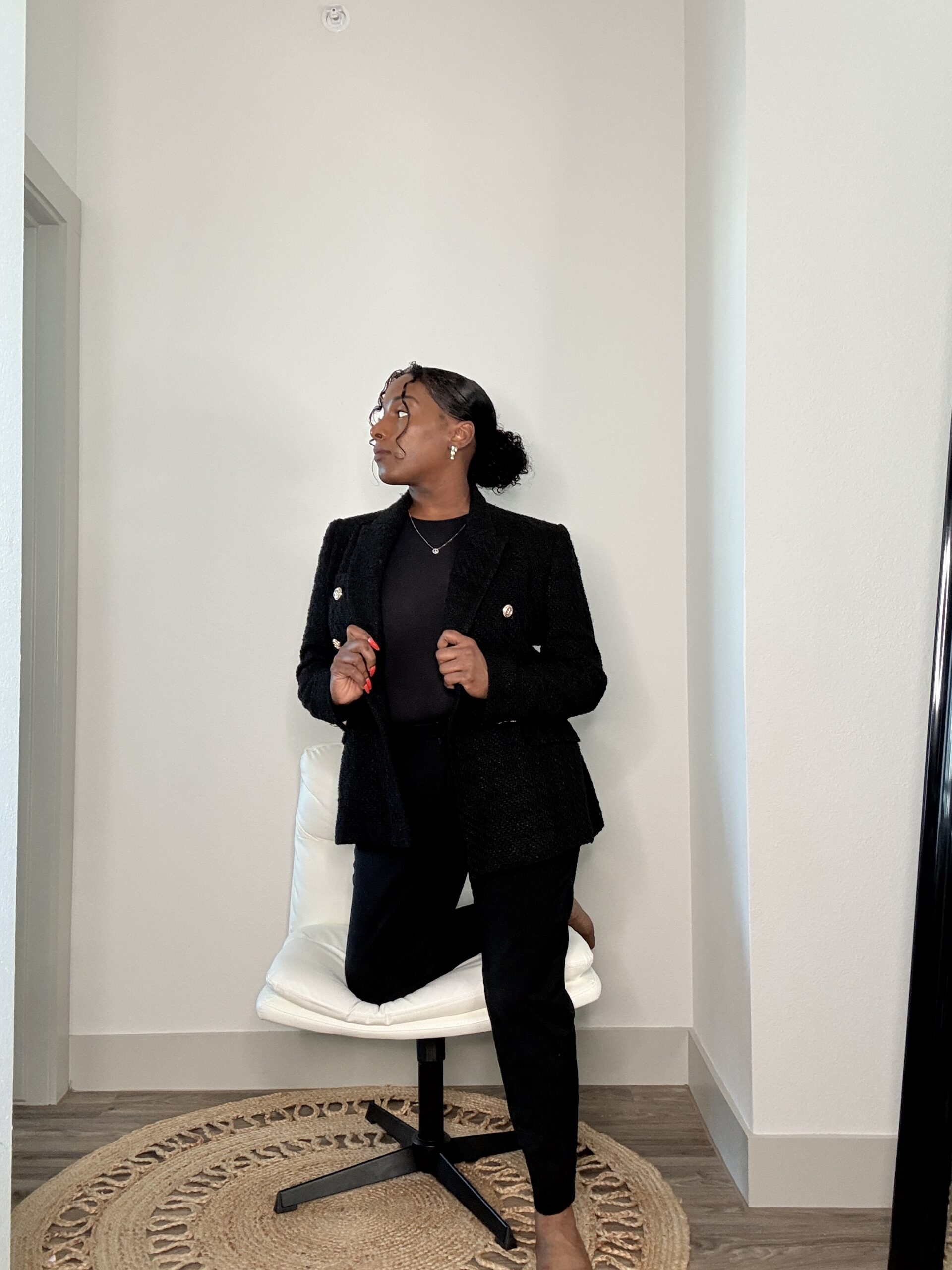 Image of Erin Nicole in black suit looking left with leg in white chair.